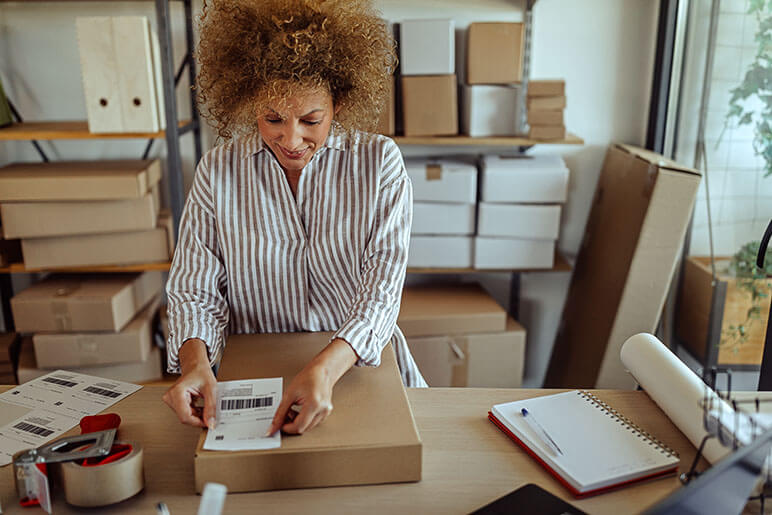 A woman putting a shipping label on a cardboard box for her business