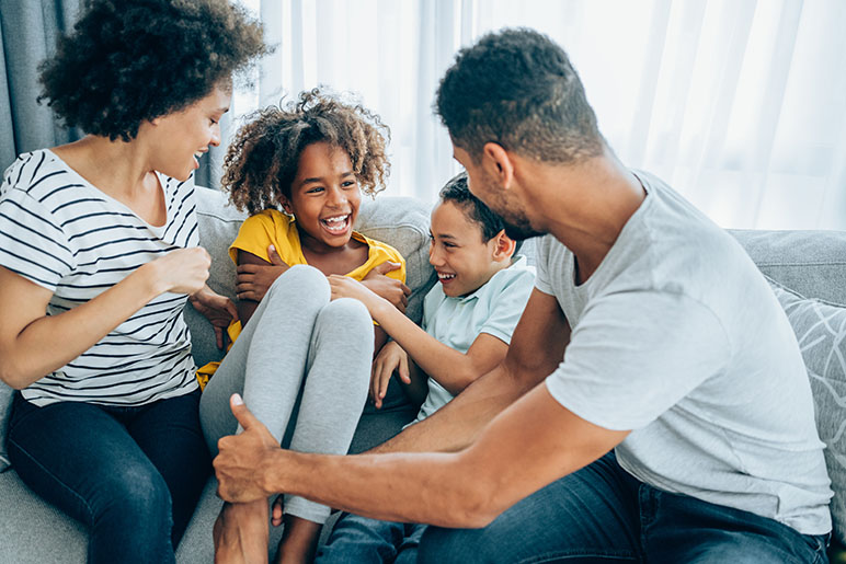 Family of four sitting on the couch laughing and smiling together a mom, dad, daughter and son