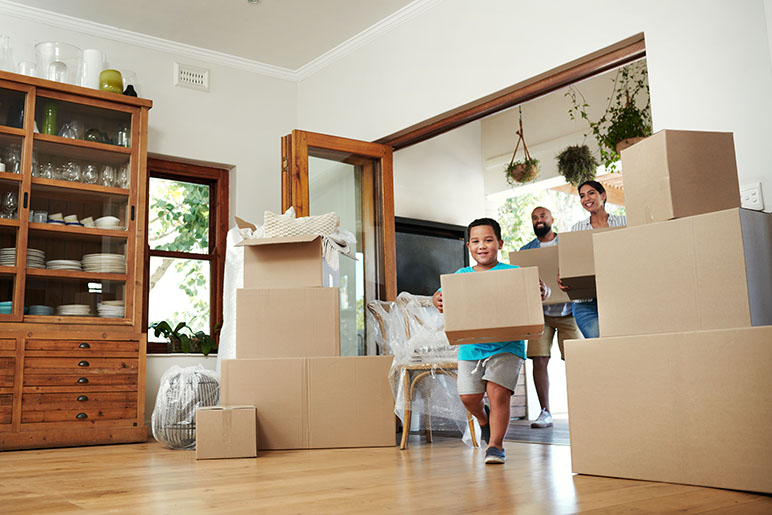 Family of four walking into their new house with cardboard boxes full of their things