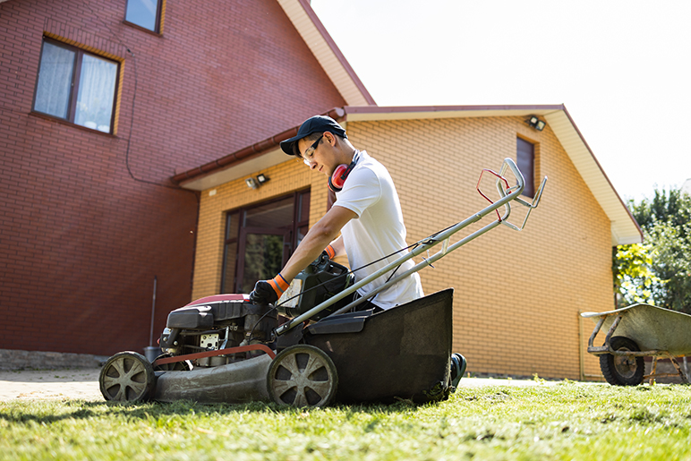 Man in lawn mower safety gear checks lawn mower