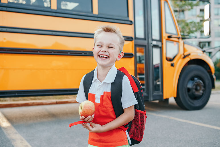 Little boy standing in front of a yellow school with an apple in his hand