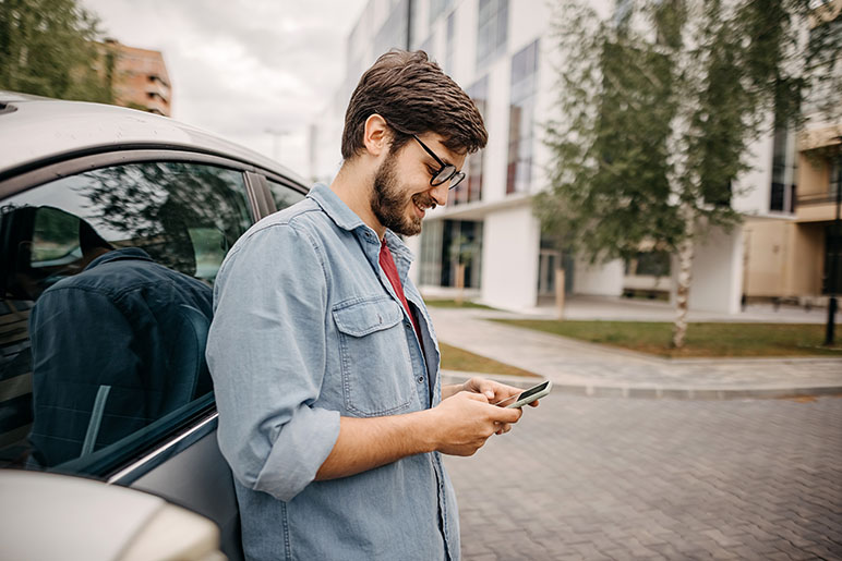 Man standing against his car looking down using his phone