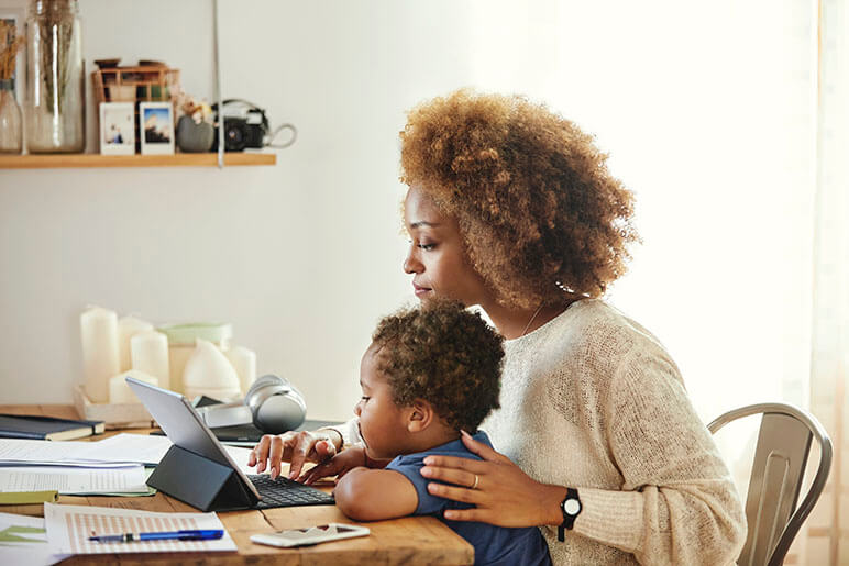 Mother and son sitting at a kitchen table looking at the women's tablet doing work