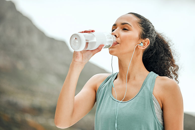 Woman drinking water bottle with headphones in while exercising in the summer