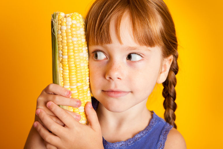 Young girl with braids holding a cob of corn