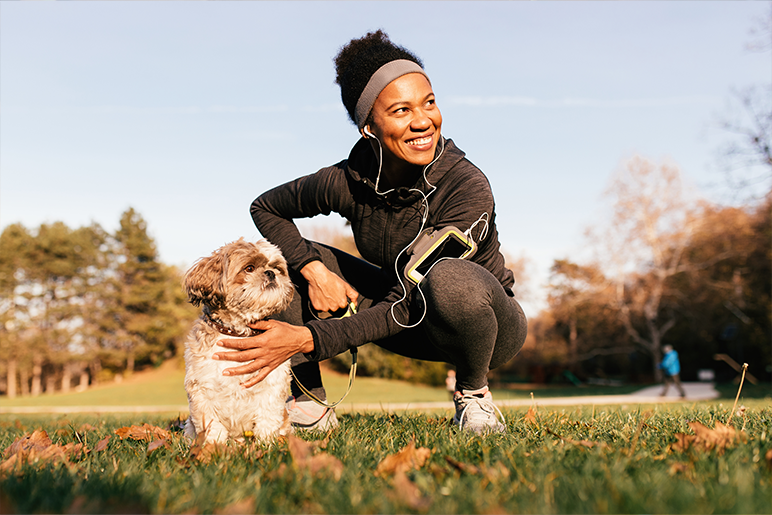 Young woman with her dog at a park with headphones on