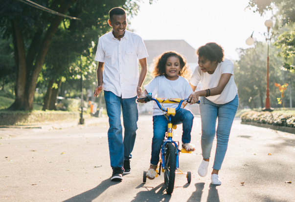 Parent helping daughter ride the bicycle in white shirt blue jean